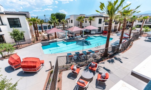 The pool area at our apartments for rent in Palm Desert, featuring beach chairs, umbrellas, and outdoor tables.